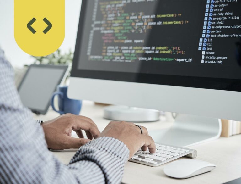 Ein Programmierer schreibt Website Code am Computer. Über dem Bild befindet sich ein Code-Symbol, bestehend aus zwei spitzen Klammern.
